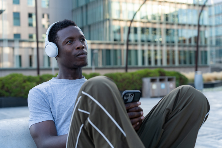 Young man enjoying music with headphones in an urban setting, holding a smartphone and looking away